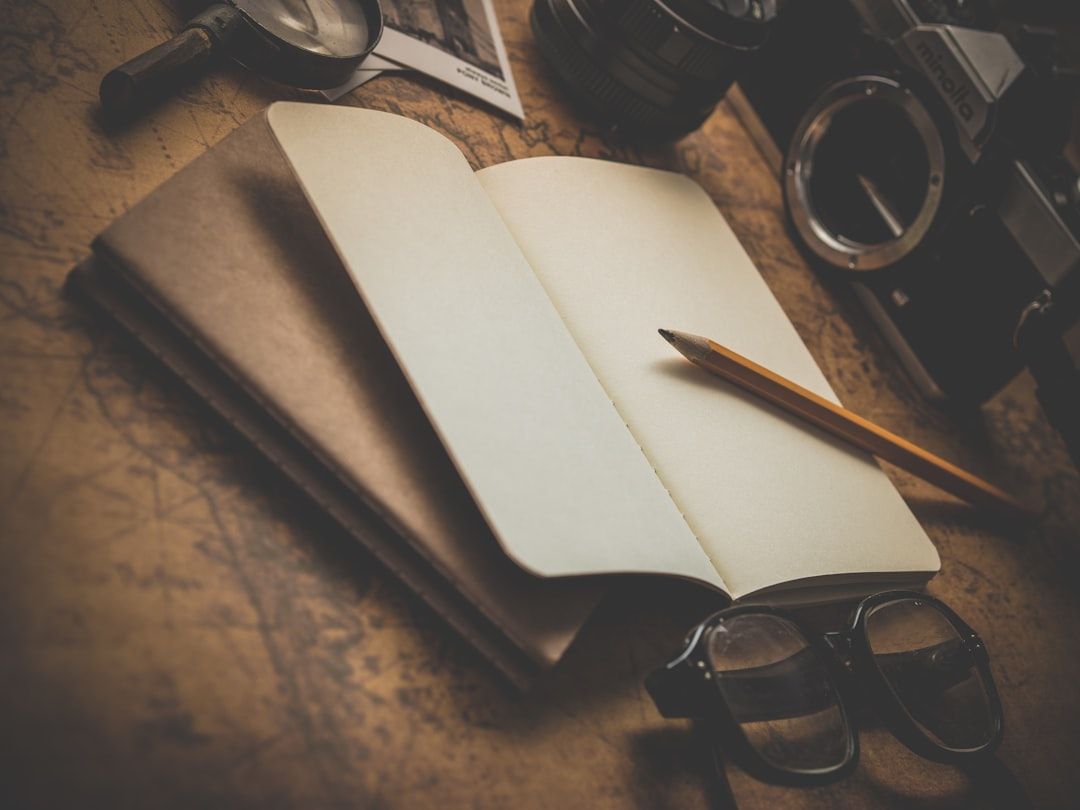 Aufgeschlagenes Notizbuch mit Bleistift auf einem Tisch, umgeben von einer Kamera, einer Brille, einer Lupe und einem Foto, das den historischen Charme Aachens einfängt.
