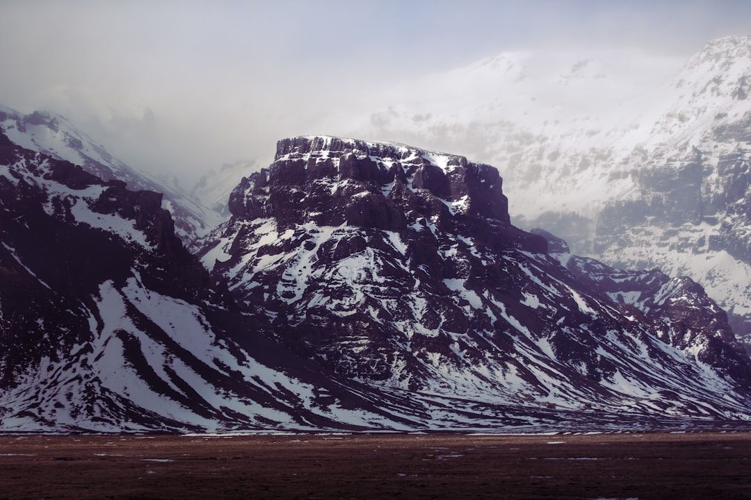 Ein großer, schneebedeckter Berg mit flacher Spitze und schroffen Flanken steht inmitten einer nebelverhangenen Landschaft, die den spektakulären Landschaften um Aachen ähnelt.
