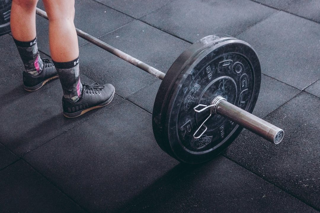 Person steht neben einer mit Gewichten beladenen Hantel, die zum Heben auf dem Boden eines Fitnessstudios in Aachen vorbereitet wird.