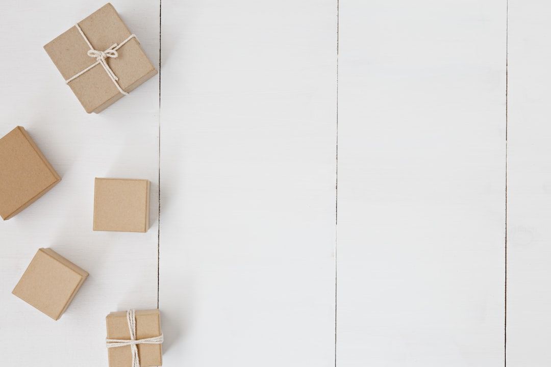 Fünf kleine braune Geschenkboxen mit Kordelbändern sind auf einer weißen Holzfläche angeordnet. Vier Boxen stehen links, eine rechts und in der Mitte ist viel Leerraum, der an einen ruhigen Aachener Marktplatz erinnert.