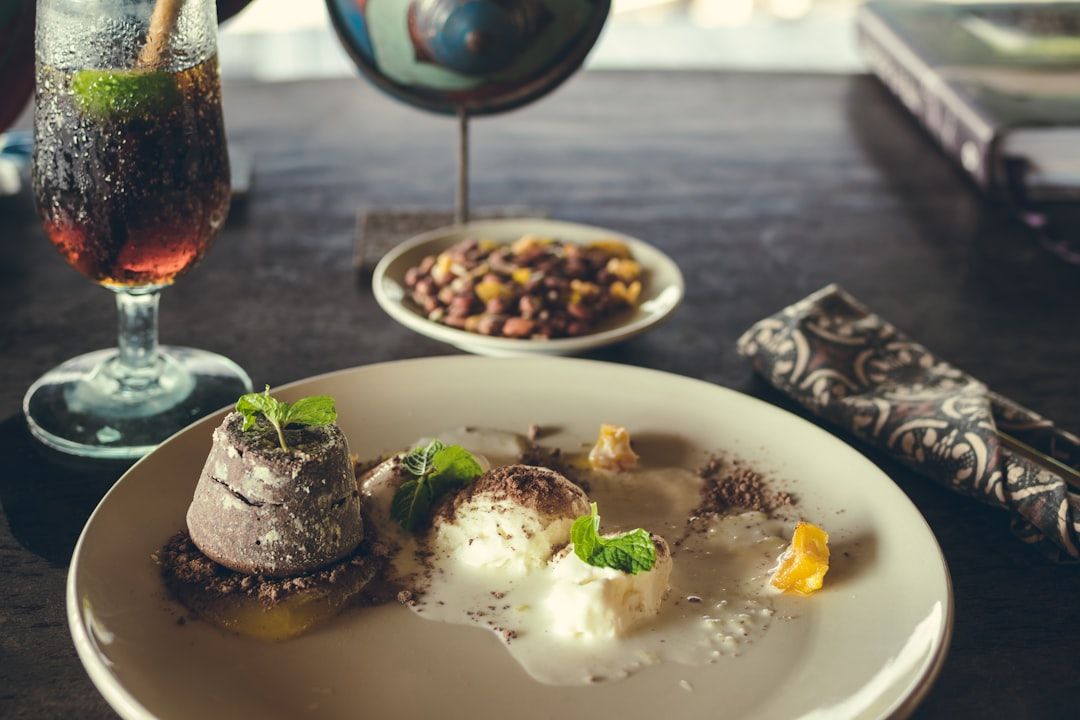 Ein Teller mit verschiedenen Desserts, garniert mit Minzblättern, dazu ein Glas Limonade und eine Schale mit gemischten Nüssen auf einem Esstisch, erinnert an die köstlichen Leckereien, die man in Aachen findet.