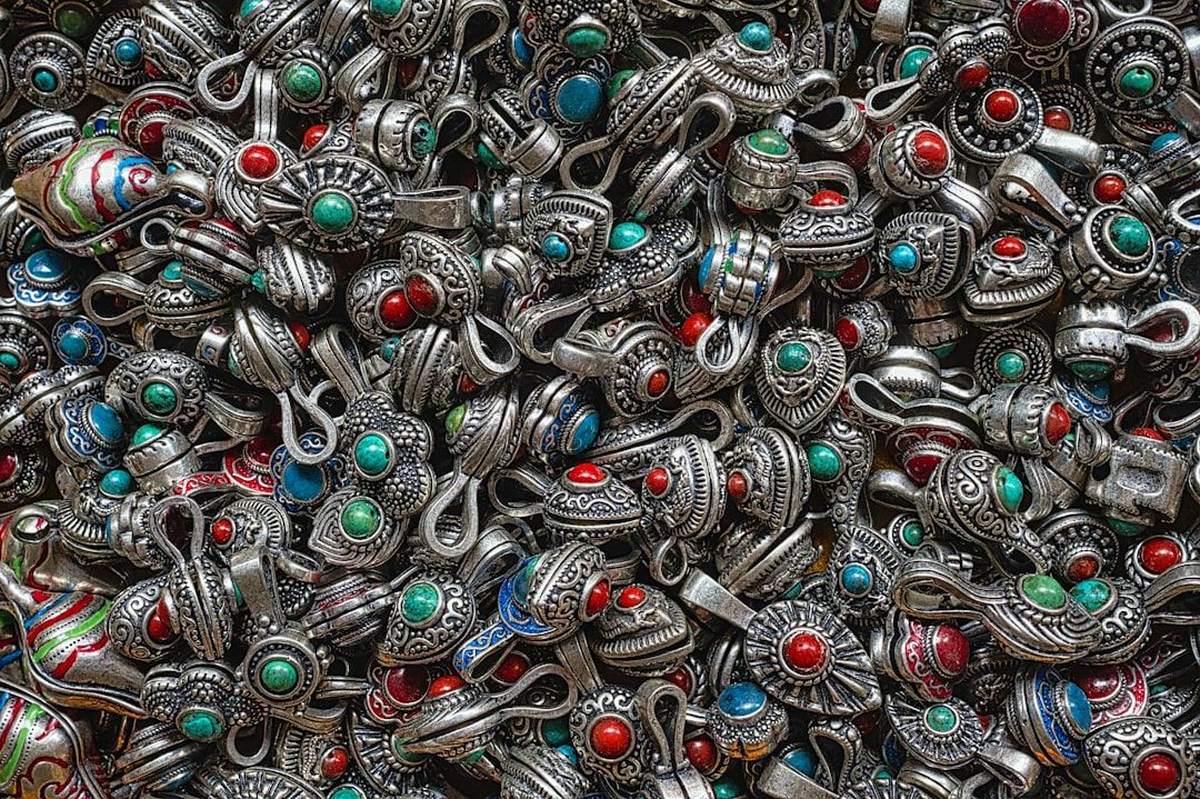 Eine Sammlung filigraner Silberschmuckstücke, verziert mit roten, grünen und blauen Steinen, die dicht an dicht aufeinander gestapelt an die exquisite Handwerkskunst Aachens erinnern.