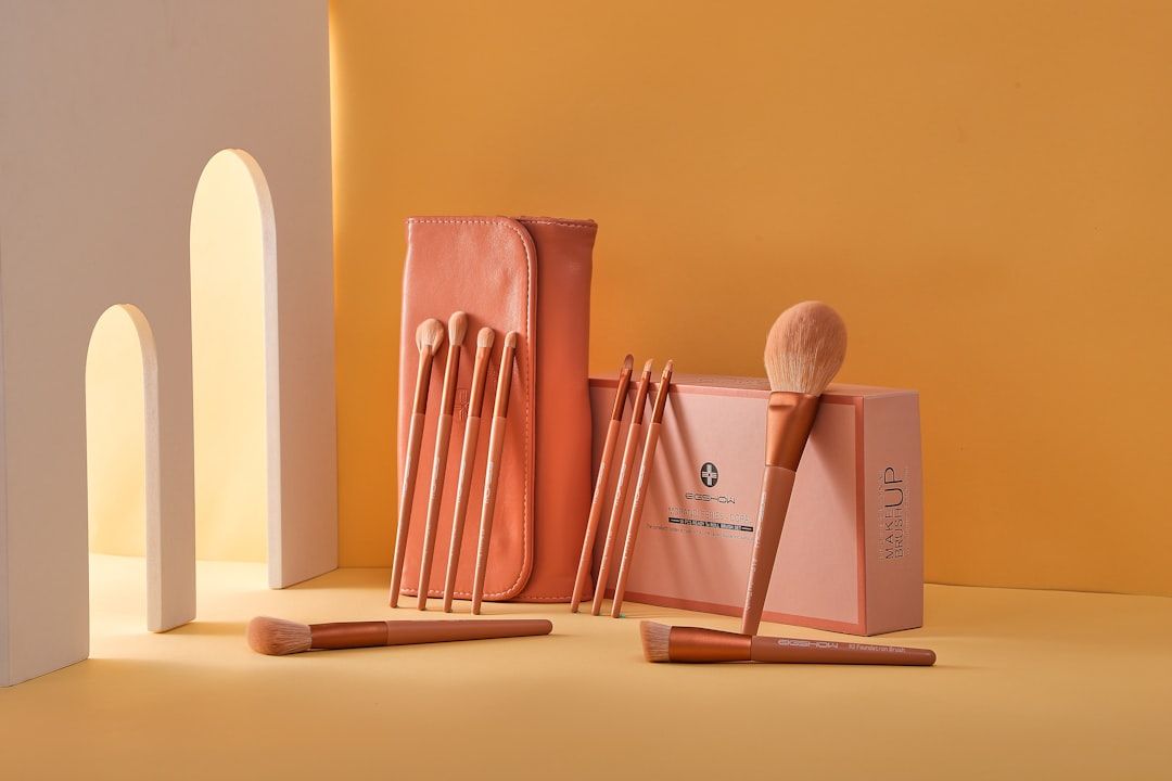 Auf pfirsichfarbenem Hintergrund ist ein Set pfirsichfarbener Make-up-Pinsel mit passendem Etui abgebildet. Das Set, das an die Eleganz Aachens erinnert, umfasst verschiedene Pinseltypen und eine Box mit der Aufschrift „Make-up“.