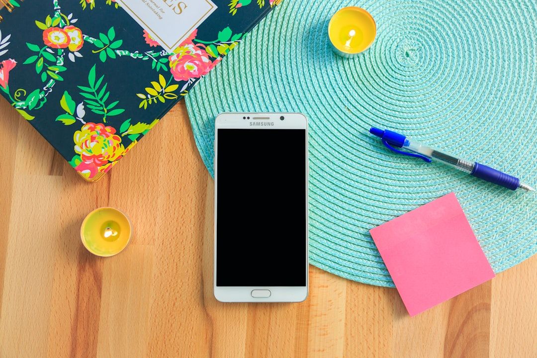 Auf einem Tisch liegt ein Smartphone, umgeben von einem geblümten Notizbuch, brennenden Kerzen, einem Aachen-Reiseführer, einem blauen Tischset und einem rosa Haftnotizzettel.