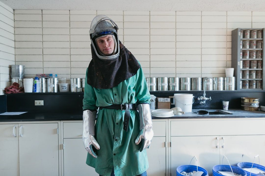 Eine Person in Schutzkleidung und Helm steht in einer Laborumgebung in Aachen, im Hintergrund sind Regale voller Behälter und Eimer auf dem Boden zu sehen.