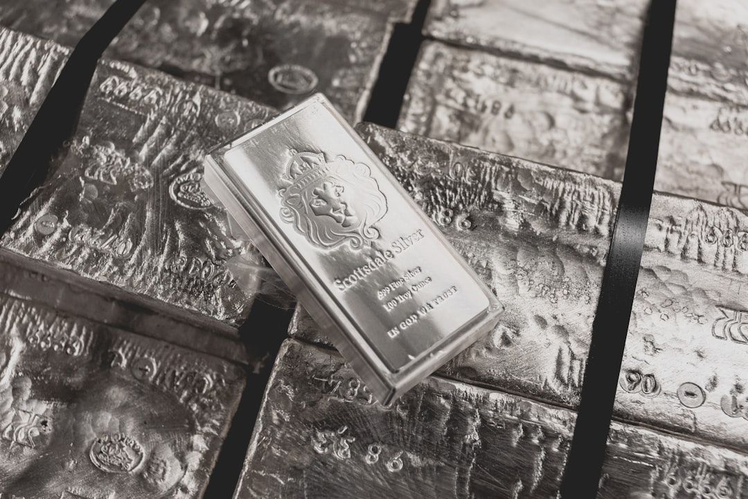 Ein polierter Silberbarren mit der Aufschrift „Scottsdale Silver“ liegt auf einem Stapel rauer, unbeschrifteter Aachener Silberbarren, die mit schwarzen Bändern zusammengebunden sind.