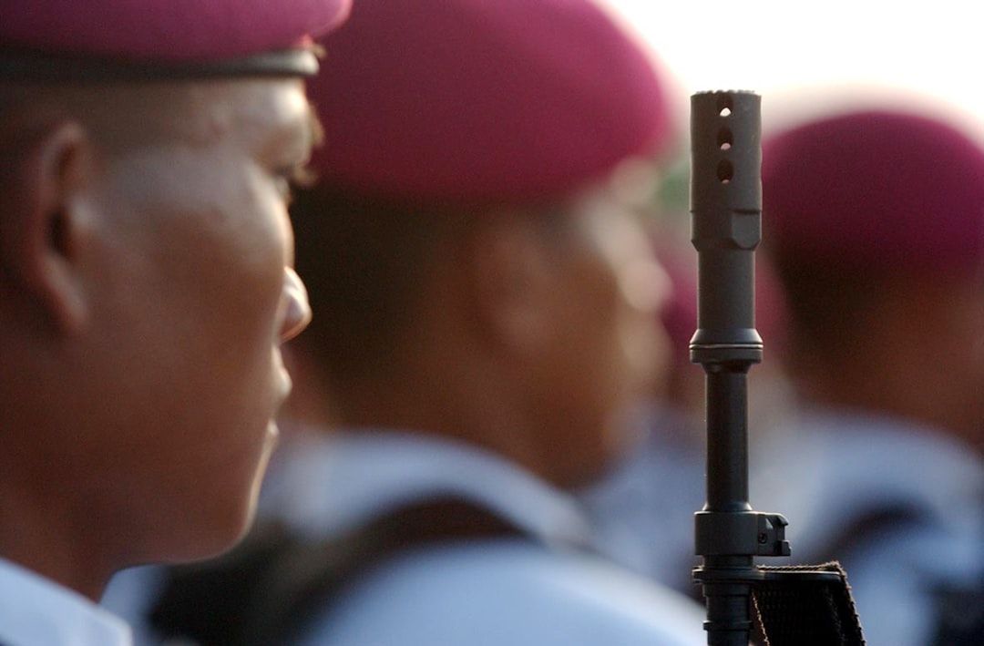 Nahaufnahme eines Soldaten mit rosa Baskenmütze und Gewehr, der mit anderen Soldaten in der Nähe von Aachen in einer Reihe steht. Alle tragen ähnliche Kleidung.