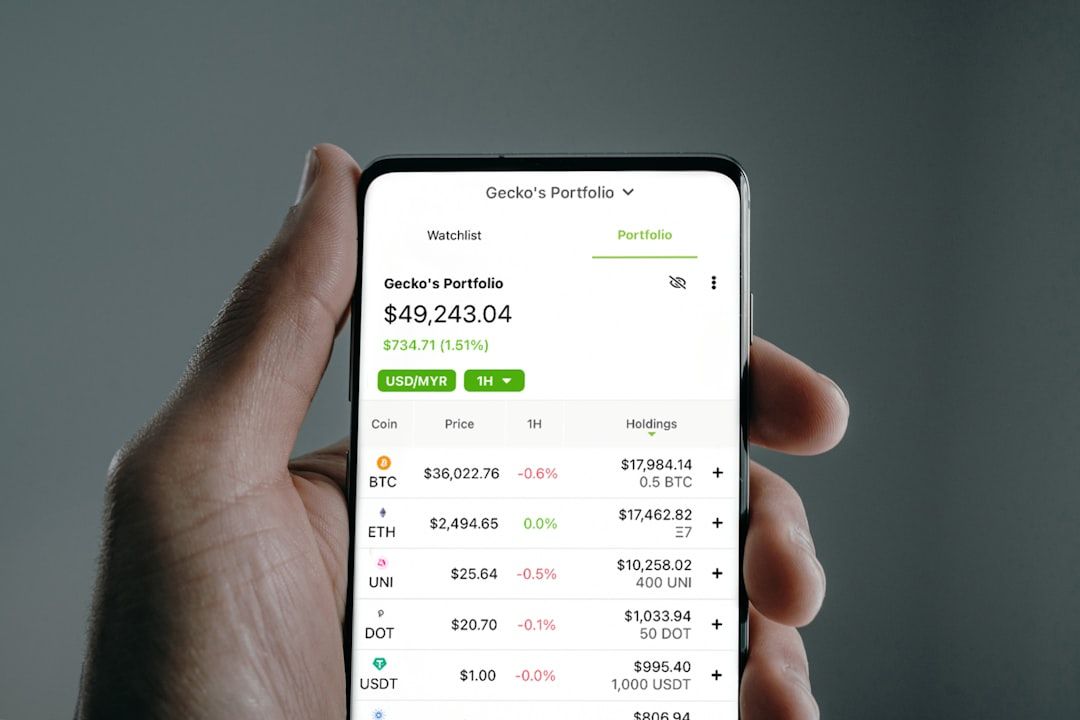 Eine Hand hält ein Smartphone, auf dem ein Kryptowährungsportfolio angezeigt wird, während sie in Aachen steht. Der Portfoliosaldo beträgt 49.243,04 $ und zeigt Bestände und aktuelle Werte für verschiedene Kryptowährungen, darunter BTC, ETH und UNI.