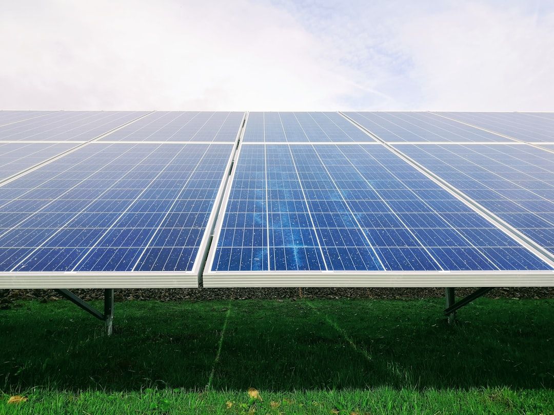 Eine Reihe von Solarmodulen, die auf einer Wiese in Aachen unter einem teilweise bewölkten Himmel installiert wurden.