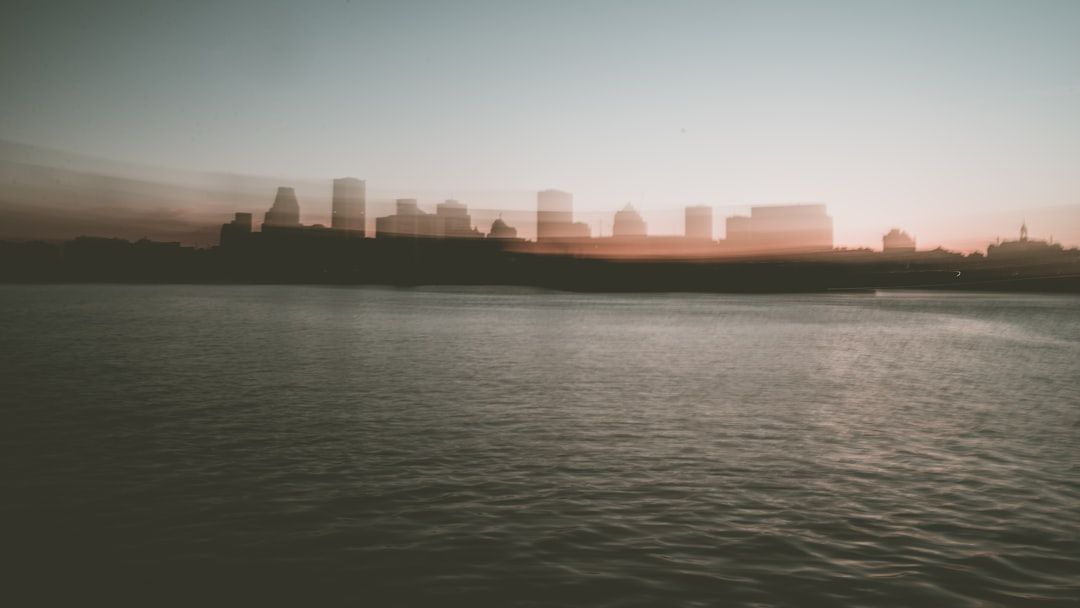 Verschwommene Skyline der Stadt bei Sonnenuntergang mit hohen Gebäuden und ruhigem Wasser im Vordergrund, erinnert an die heiteren Abende Aachens.