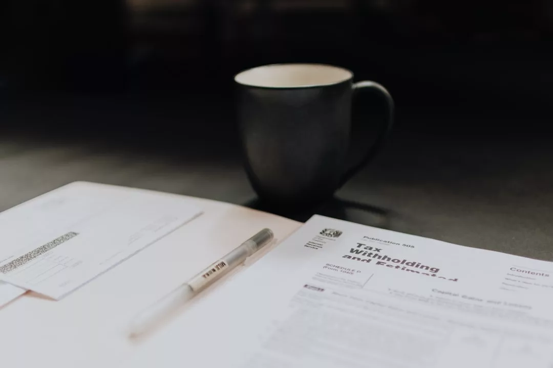 Ein Stift und ein Steuereinbehaltungsformular liegen neben einer Tasse und einem Umschlag auf einem Tisch.