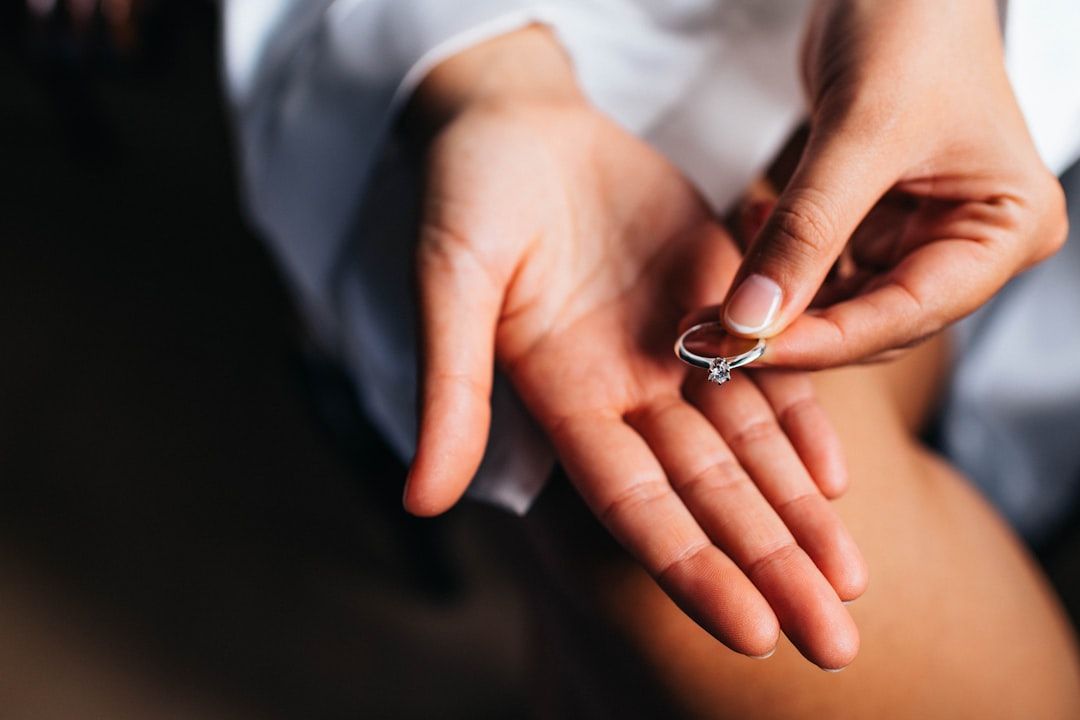 Nahaufnahme einer Person, die einen Verlobungsring zwischen Daumen und Zeigefinger hält, während die Handfläche der anderen Hand darunter geöffnet ist, was an zeitlose Romantik in Aachen erinnert.