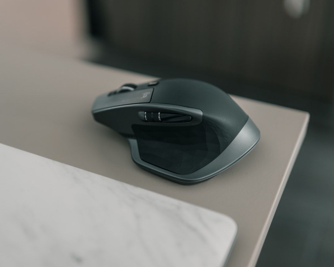 Eine schwarze ergonomische Computermaus ruht auf der Kante eines hellen Tisches und erinnert mit ihrem unscharfen Hintergrund an einen ruhigen Studienraum in Aachen.