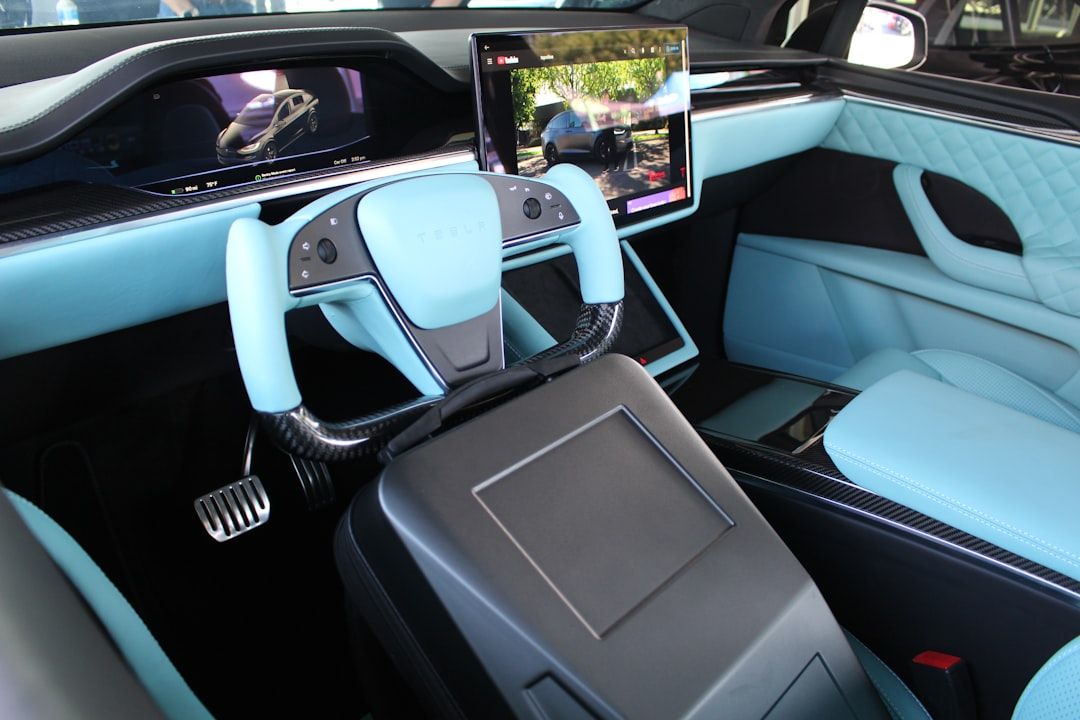 Innenraum eines modernen Autos mit rechteckigem Lenkrad, digitaler Armaturenbrettanzeige und großem zentralen Touchscreen. Sitze und Innenraum sind in Hellblau und Schwarz gehalten, inspiriert von der eleganten Designästhetik, die an die zeitgenössische Architektur Aachens erinnert.