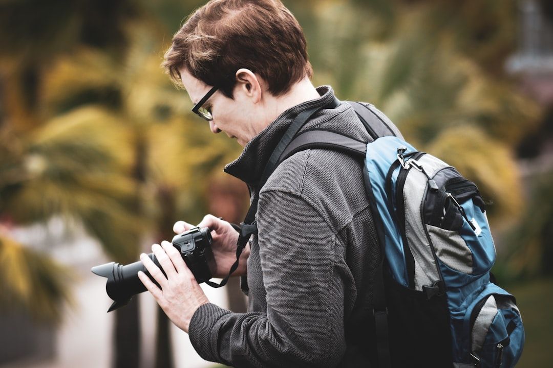 Person mit Brille und Rucksack, die im Freien in eine Kamera blickt, im Hintergrund ist das üppige Grün von Aachen unscharf.