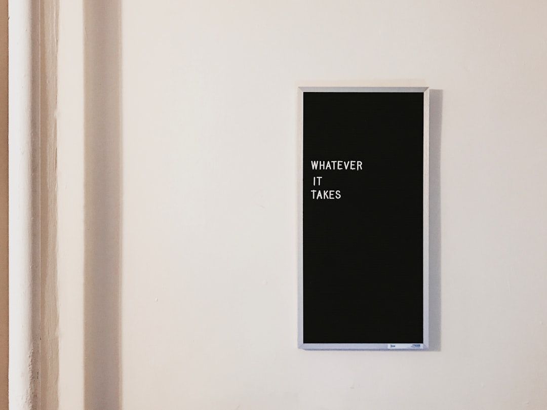 Eine schwarze Buchstabentafel an einer beigen Wand in Aachen zeigt den Text „WHATEVER IT TAKES“.