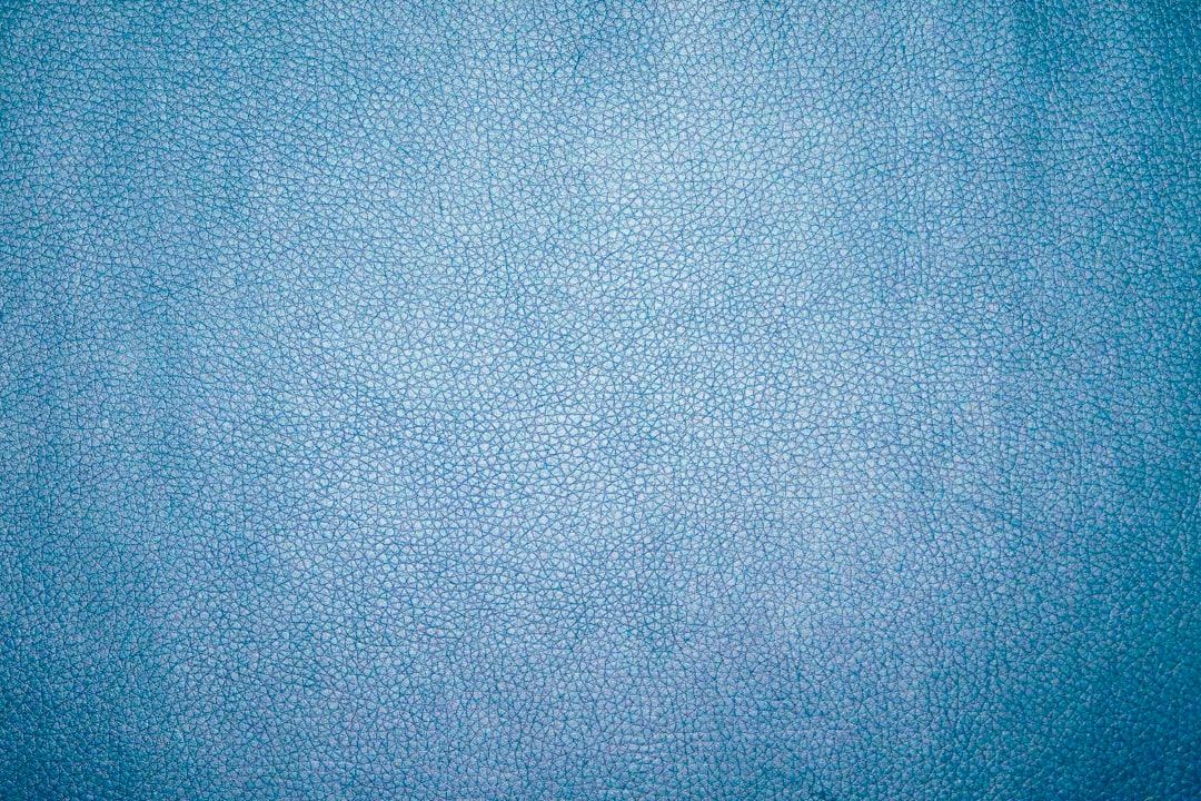Nahaufnahme der Textur von blauem Leder mit einem feinen, gesprenkelten Muster, das an die Eleganz von Aachen erinnert. Die Oberfläche hat einen subtilen Glanz und eine gleichmäßige Farbe.
