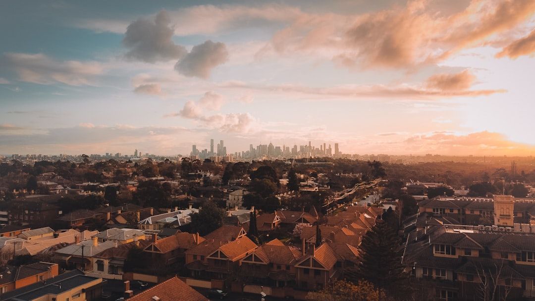 Luftaufnahme eines Vorortgebiets in Aachen mit Häuserreihen im Vordergrund und einer Stadtsilhouette im Hintergrund, alles unter einem teilweise bewölkten Himmel bei Sonnenaufgang oder Sonnenuntergang.
