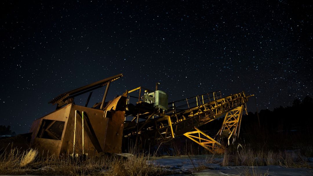 Eine verrostete, verlassene Industriemaschine steht auf einem Feld unter einem sternenklaren Nachthimmel, wie ein Relikt aus Aachens vergangener Zeit.