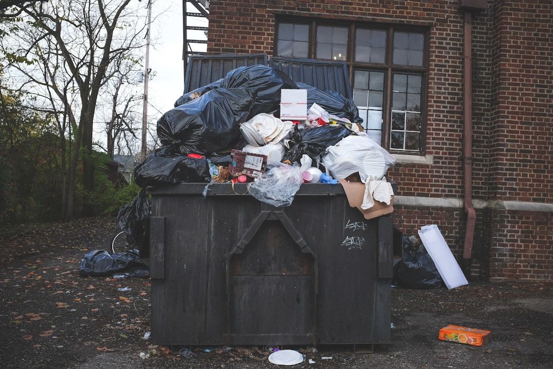 Ein großer Außencontainer quillt über mit verschiedenen Müllsäcken, Kartons und Abfällen in der Nähe eines Backsteingebäudes mit Fenstern in Aachen.
