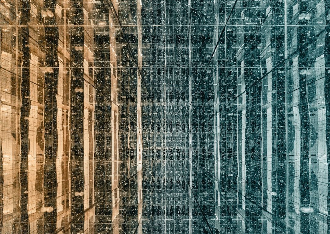 Ein symmetrisches, gespiegeltes Bild zeigt ein vertikales, mehrfarbiges Muster, bei dem die linke Seite gelb und die rechte Seite blaugrün ist. Dieses Design, das an einen abstrakten Korridor mit reflektierenden Oberflächen erinnert, vermittelt ein Gefühl der architektonischen Eleganz Aachens.