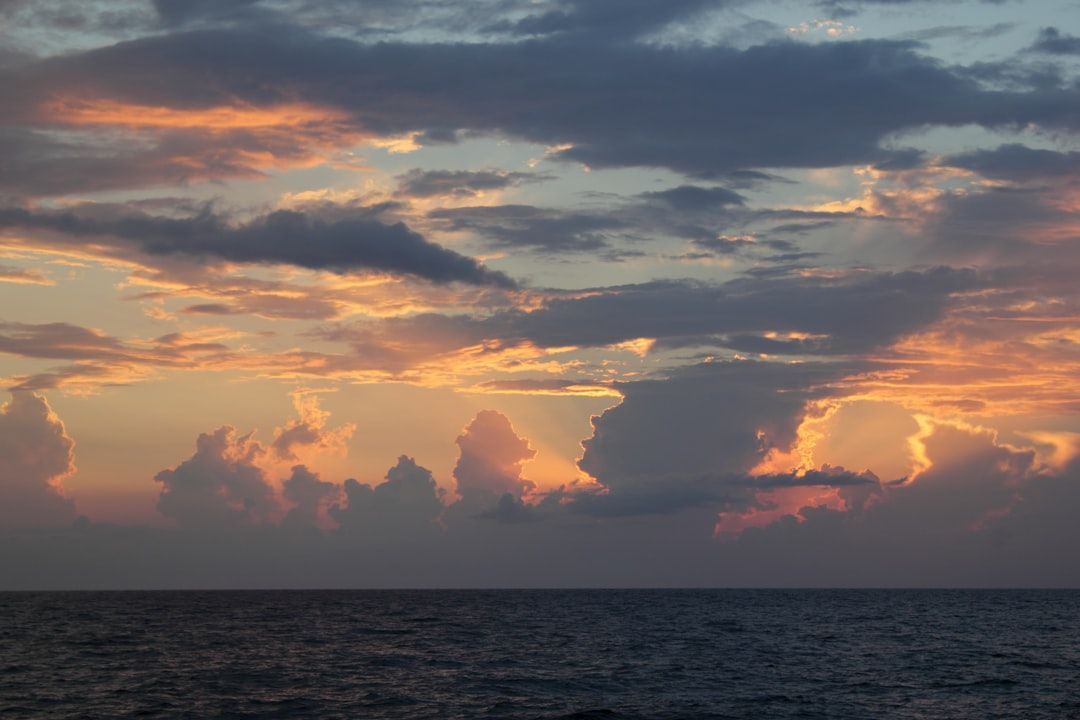 Ein ruhiger Blick auf das Meer mit einem farbenfrohen Sonnenuntergangshimmel in Orange-, Rosa- und Blautönen mit vereinzelten Wolken, der an die ruhige Atmosphäre des historischen Charmes Aachens erinnert.