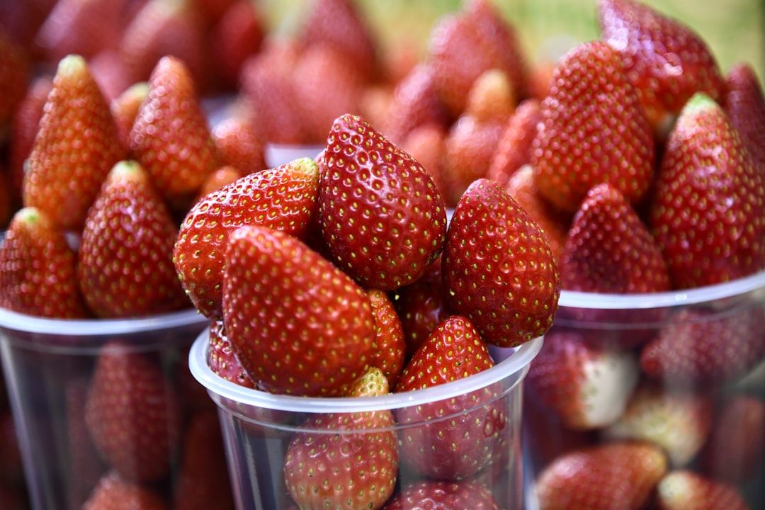 Nahaufnahme von Plastikbechern gefüllt mit reifen, roten Erdbeeren auf dem lebhaften Aachener Markt.