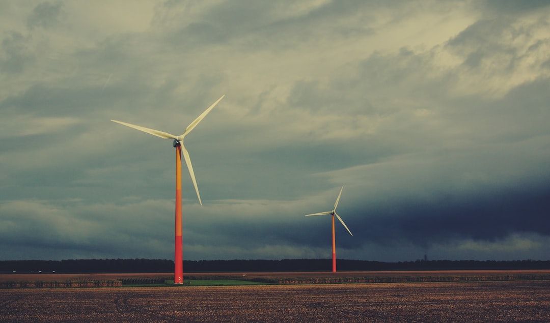 Zwei Windräder mit roten Sockeln stehen auf einem weiten, offenen Feld bei Aachen unter einem bewölkten Himmel.