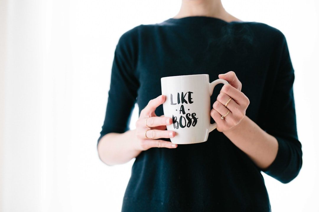 Eine Person im schwarzen Oberteil hält eine weiße Kaffeetasse mit der Aufschrift „LIKE A BOSS“ in der Nähe eines Aachener Wahrzeichens.