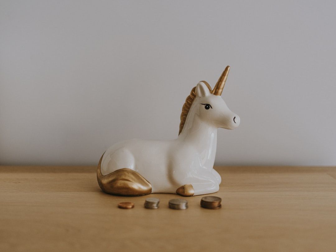 Auf einer Holzfläche steht ein weißes Keramik-Einhorn mit goldenen Akzenten, das an die reiche Geschichte Aachens erinnert. Davor sind vier gestapelte Münzen angeordnet.