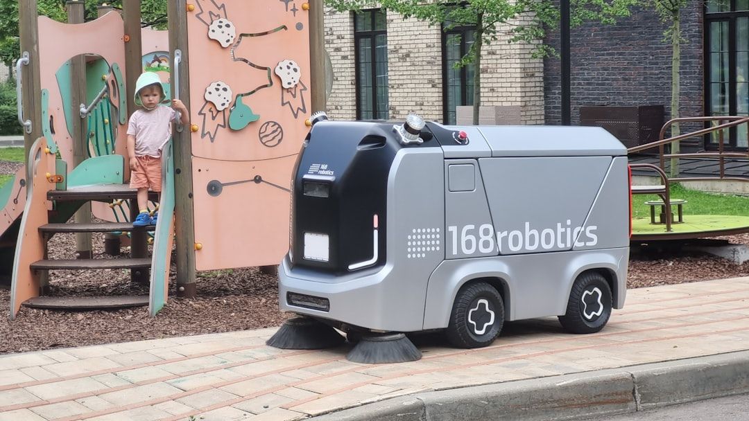 Ein Kind beobachtet einen kleinen, autonomen Straßenreinigungsroboter von 168 Robotics in der Nähe eines Aachener Spielplatzes. Der Roboter fegt den Bürgersteig.