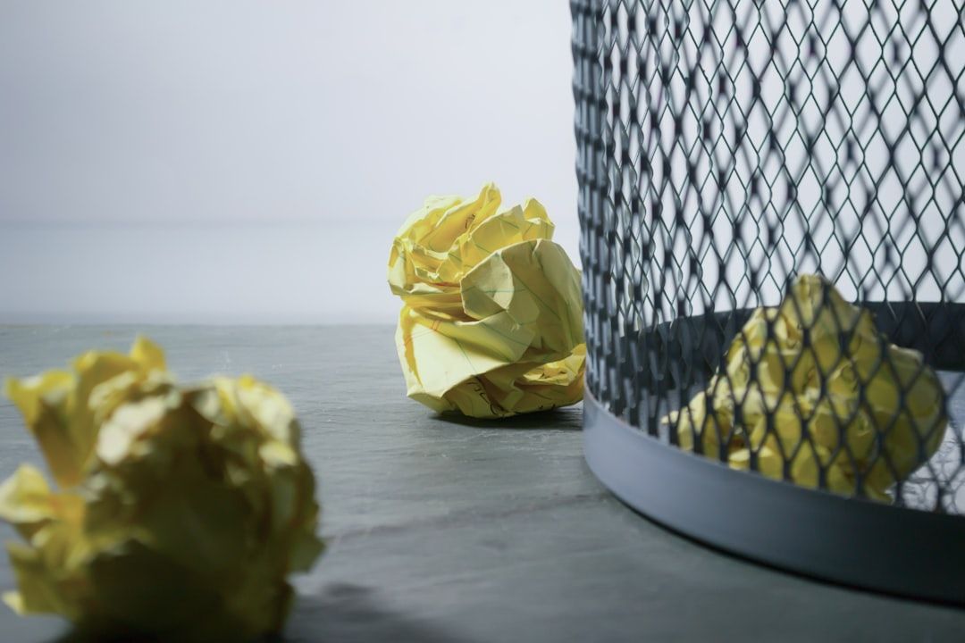 Ein Mülleimer aus Gitter, daneben drei zerknüllte gelbe Papiere auf grauem Untergrund, erinnert an ein Aachener Künstleratelier.