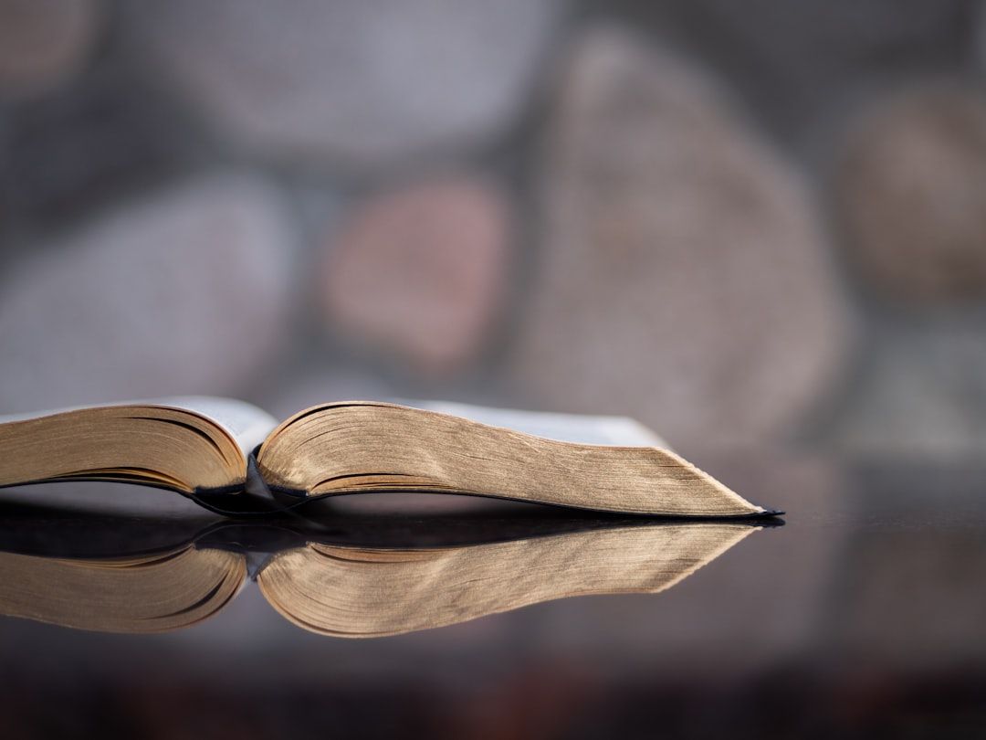 Ein offenes Buch liegt flach auf einer spiegelnden Oberfläche, im Hintergrund sind die verschwommenen Steinmauern von Aachen zu sehen.