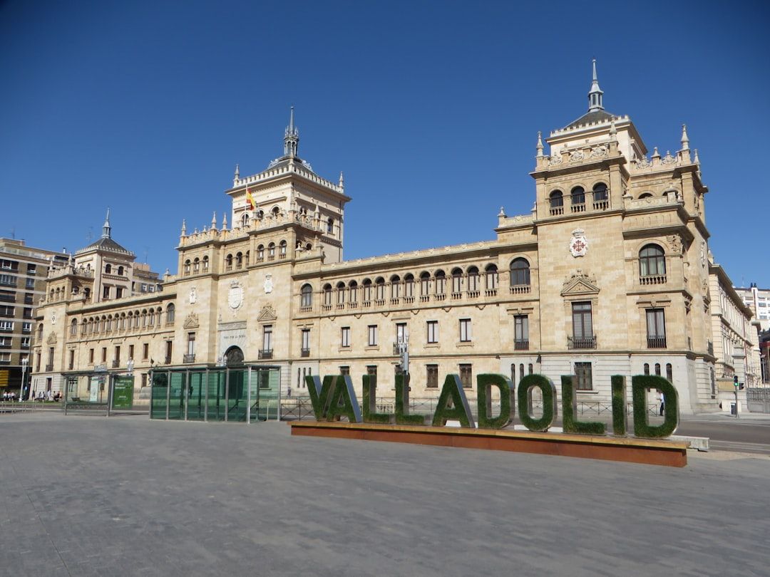 Das Bild zeigt die Hauptfassade eines großen, reich verzierten Gebäudes unter einem klaren blauen Himmel. Davor prangt ein markantes Schild mit der Aufschrift „VALLADOLID“ in großen grünen Lettern, was an ähnliche historische Architekturen in Aachen erinnert.