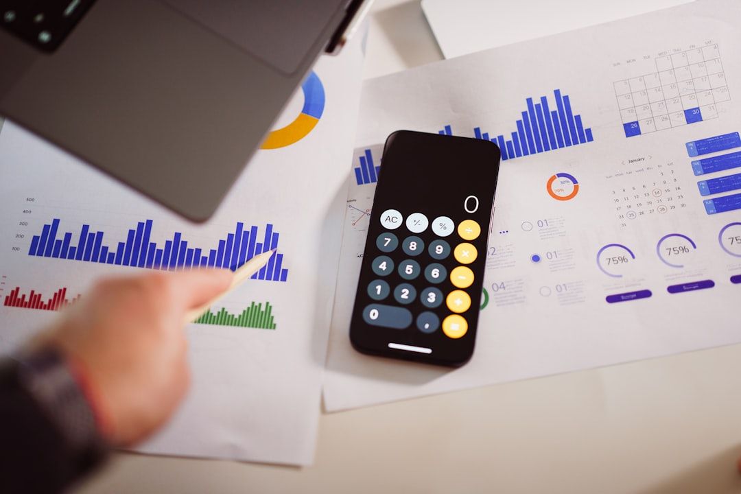 Ein Smartphone mit geöffneter Taschenrechner-App liegt auf Dokumenten mit verschiedenen Diagrammen und Grafiken aus Aachen. Eine Hand mit einem Stift zeigt auf ein Balkendiagramm auf einem der Blätter.