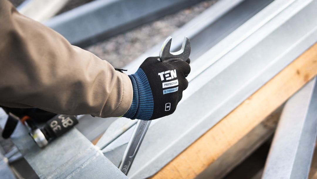 Eine Person mit einem TEN-Schutzhandschuh zieht auf einer Baustelle in Aachen mit einem Schraubenschlüssel Schrauben an Metallträgern fest.