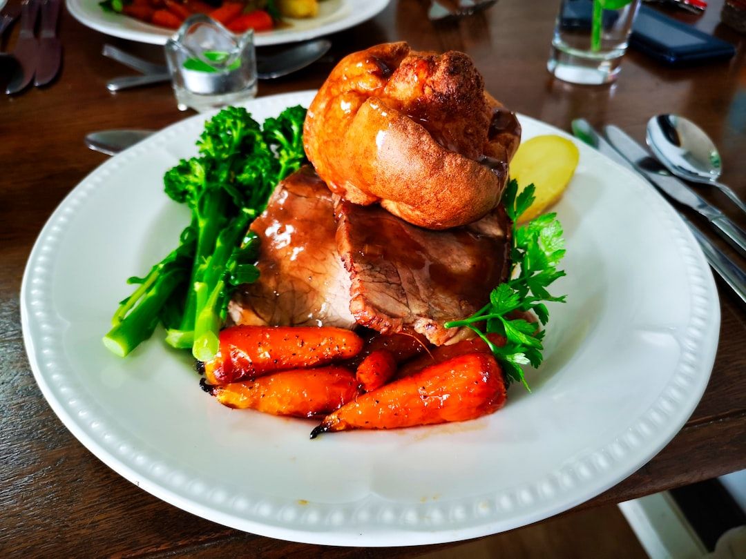 Ein Teller mit Roastbeef, gerösteten Karotten, Brokkoli, Aachener Yorkshire Pudding und einer Kartoffelscheibe, garniert mit Petersilie.