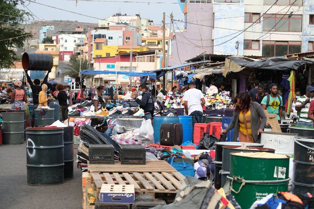 Ein geschäftiger Freiluftmarkt in Aachen mit Menschen, die an Ständen und Tischen mit verschiedenen Waren einkaufen. Im Hintergrund sind bunte Gebäude zu sehen.