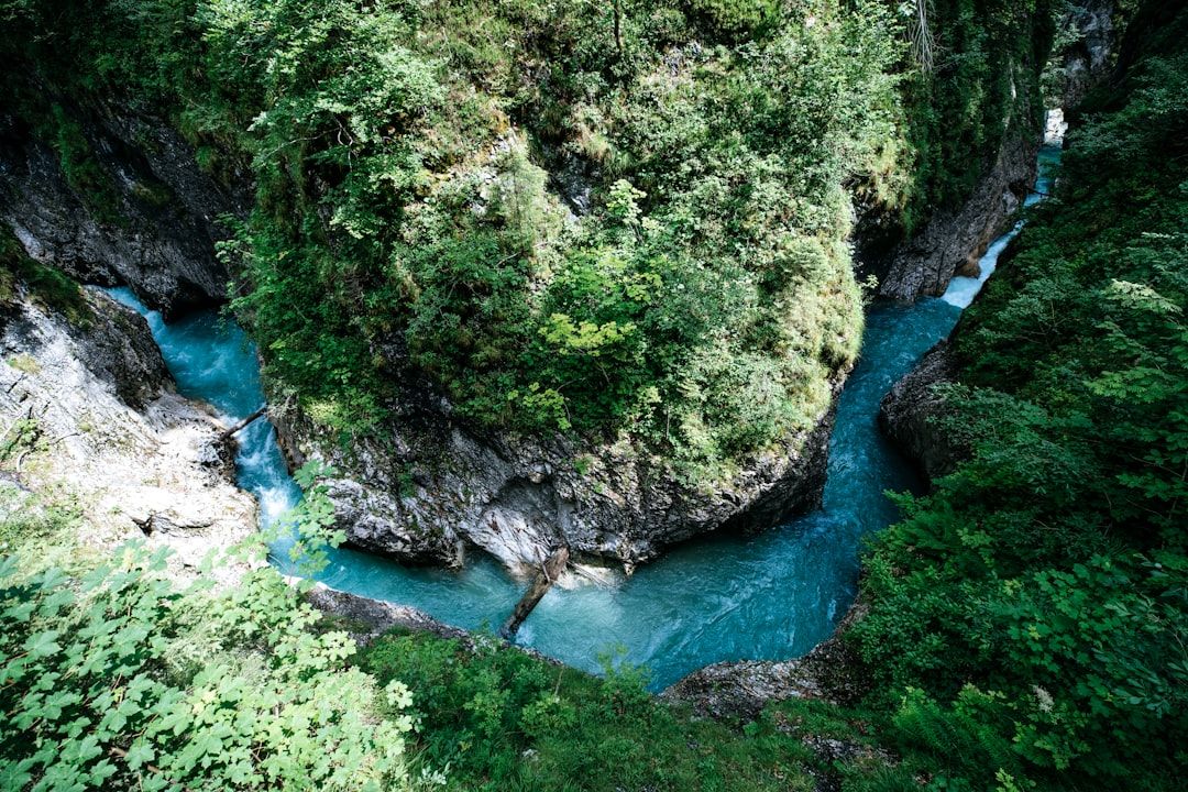 Ein schmaler, türkisfarbener Fluss fließt durch eine tiefe, felsige Schlucht bei Aachen, umgeben von dichter grüner Vegetation.