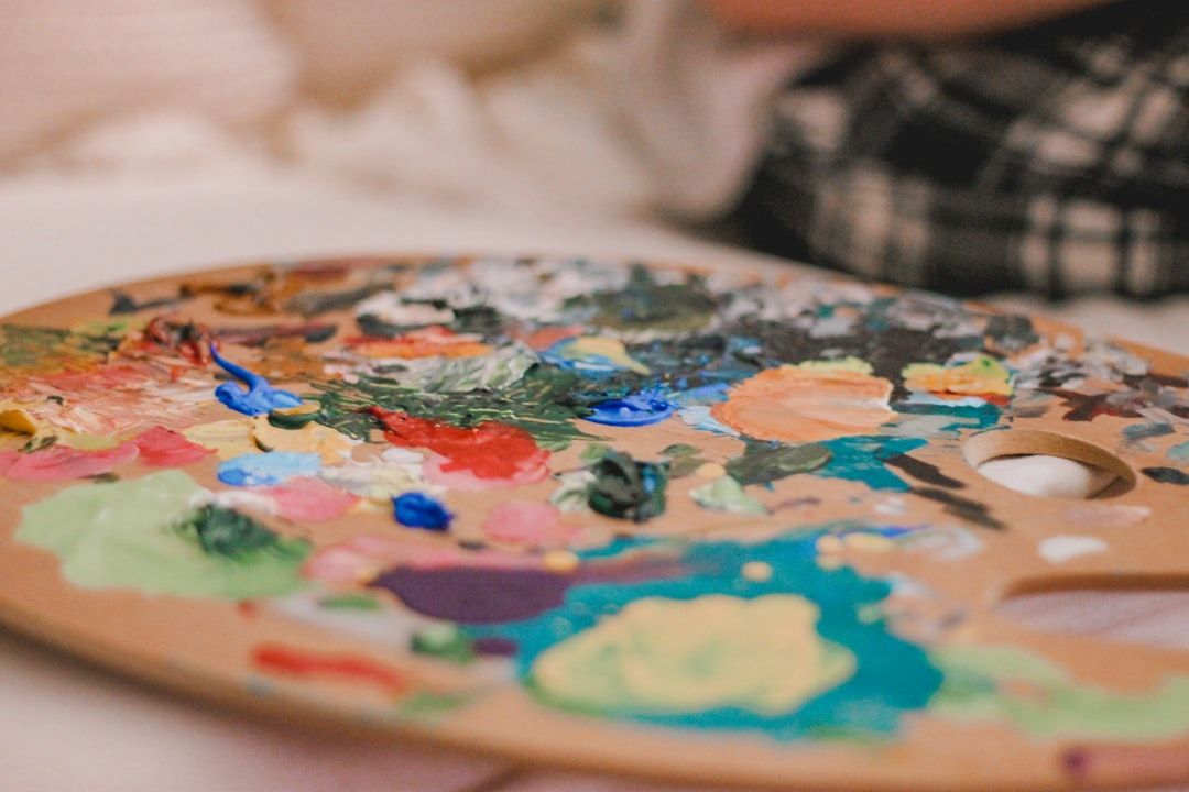 Auf einer flachen Oberfläche liegt eine hölzerne Künstlerpalette, die mit gemischten und ungemischten Farben in unterschiedlichen Schattierungen bedeckt ist und an die lebendigen Farbtöne der historischen Kunstszene Aachens erinnert.