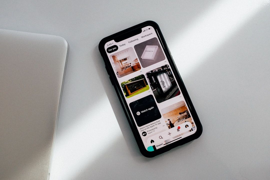 Auf dem Bildschirm eines Smartphones wird die Pinterest-App angezeigt. Das Telefon liegt auf einer weißen Oberfläche neben einem eleganten silbernen Laptop und erinnert an den modernen Charme der technisch versierten Straßen Aachens.