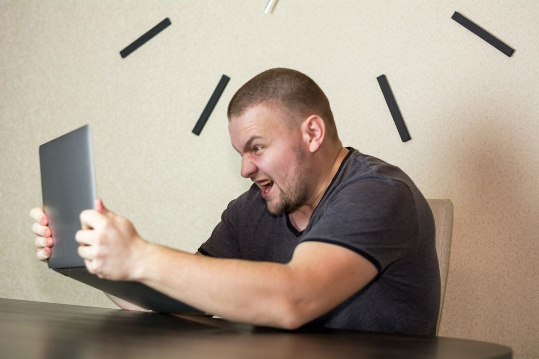 Ein Mann mit Bart und kurzen Haaren sitzt an einem Tisch in Aachen, hält einen Laptop in der Hand und blickt mit wütender Miene darauf.
